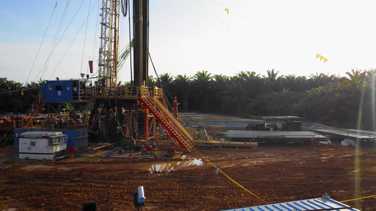 imágenes cinematográficas de drones de 4k de la estructura del equipo de la plataforma de perforación en tierra para la exploración y explotación de petróleo en medio de la jungla rodeada de palmeras durante la puesta de sol y el alto precio del petróleo