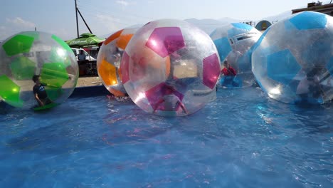 unidentified children play having fun inside large vballs on the water