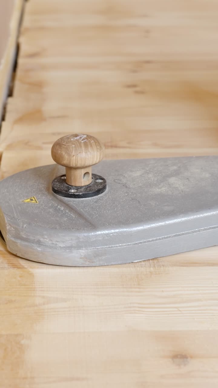 Sanding wooden floor edges with a tool in a workshop setting, vertical