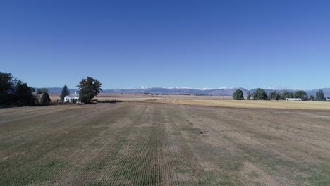 a zoom out along a corn field with a farmhouse backed by majestic mountains