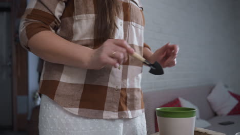 plant loving creative twirling joyfully with small shovel while working soil into planter on glass table amid lush indoor plants in bright white room radiating playful gardening energy