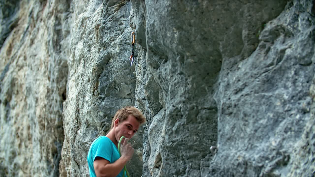 Athletic man attaching a rope to a quickdraw while preparing for rock climbing