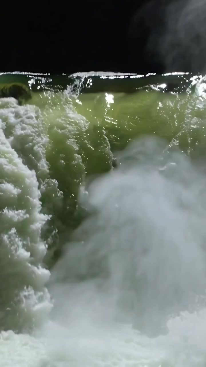 Video verticale: Un'onda che si infrange, una cortina d'acqua che si riversa sul bordo di notte, creando schiuma e spruzzi.