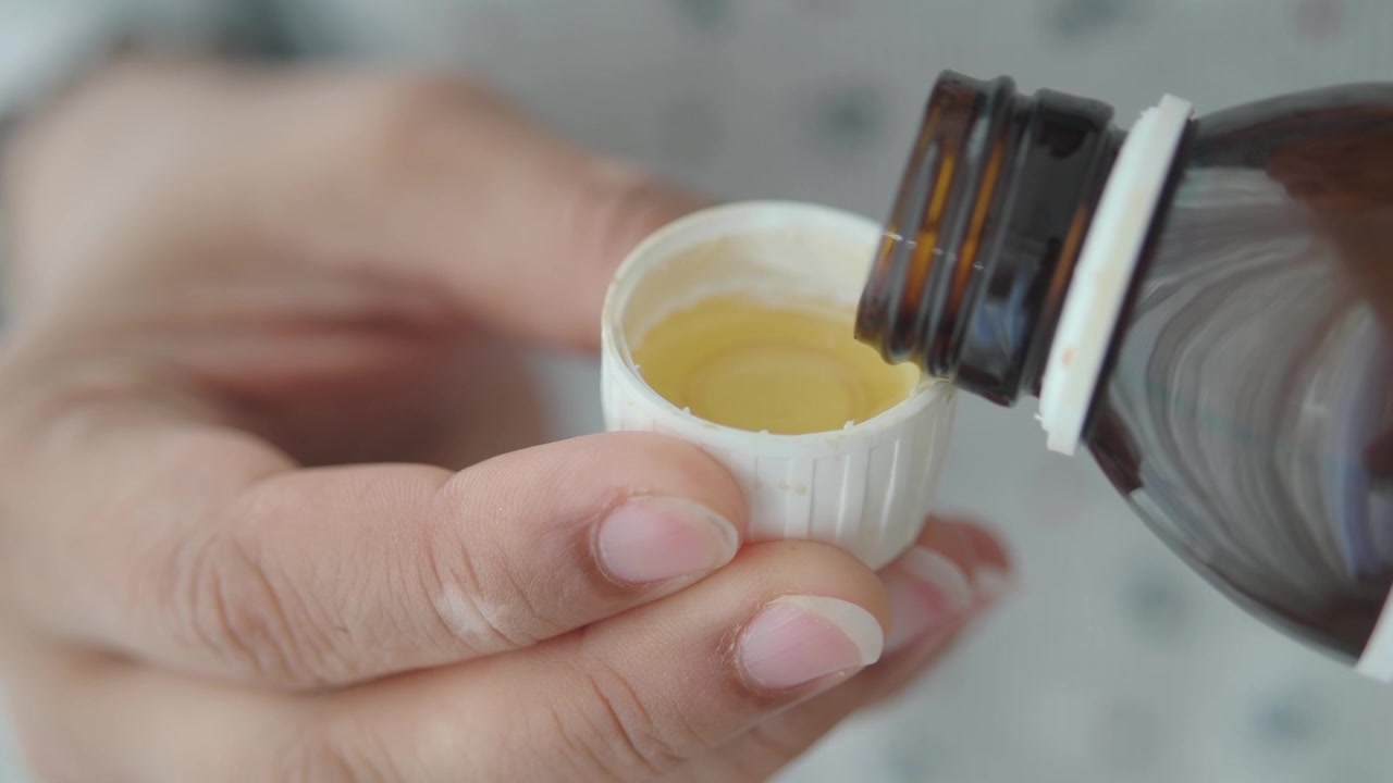 Mano vertiendo medicamento líquido en una tapa medidora
