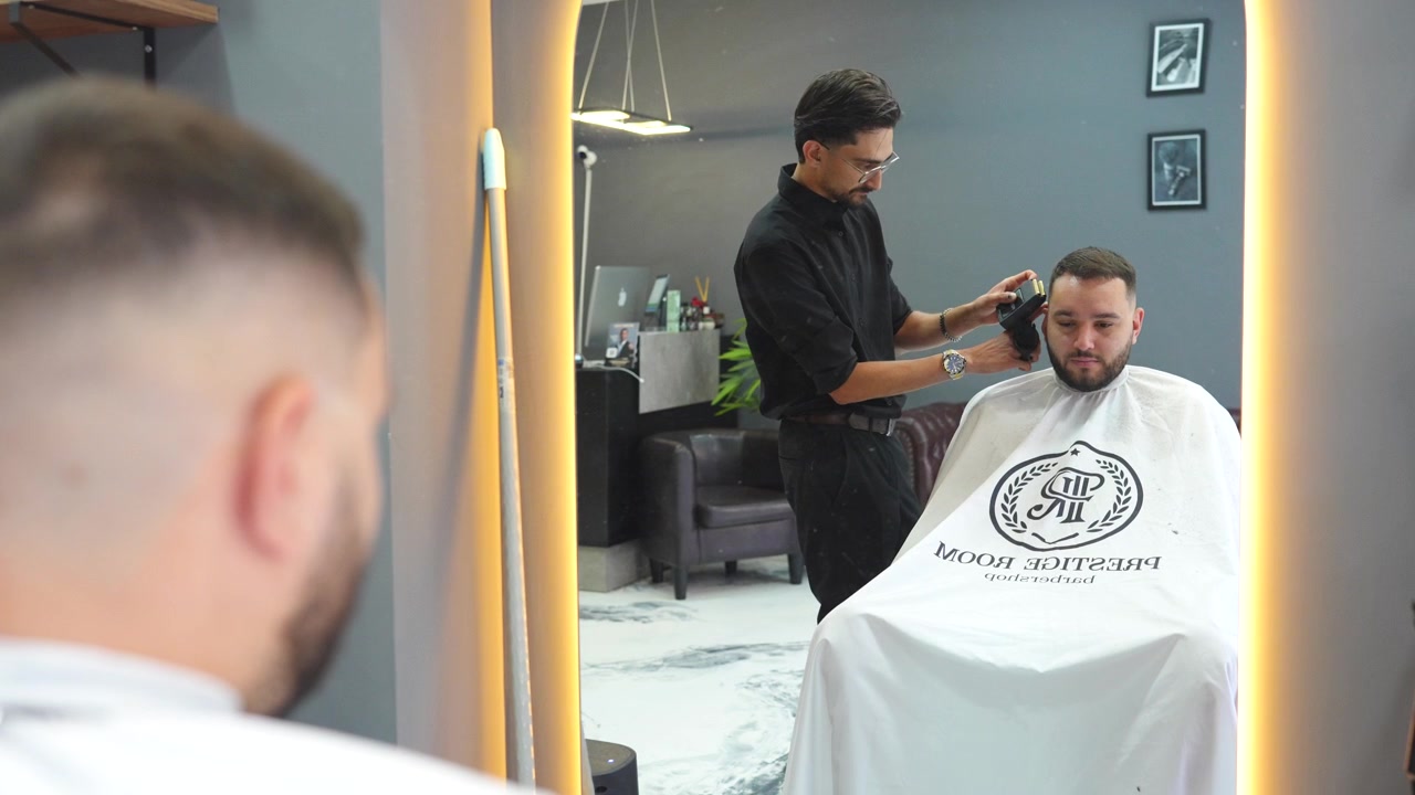 Hair stylist giving a haircut to a male client in a modern barbershop with a hair clipper