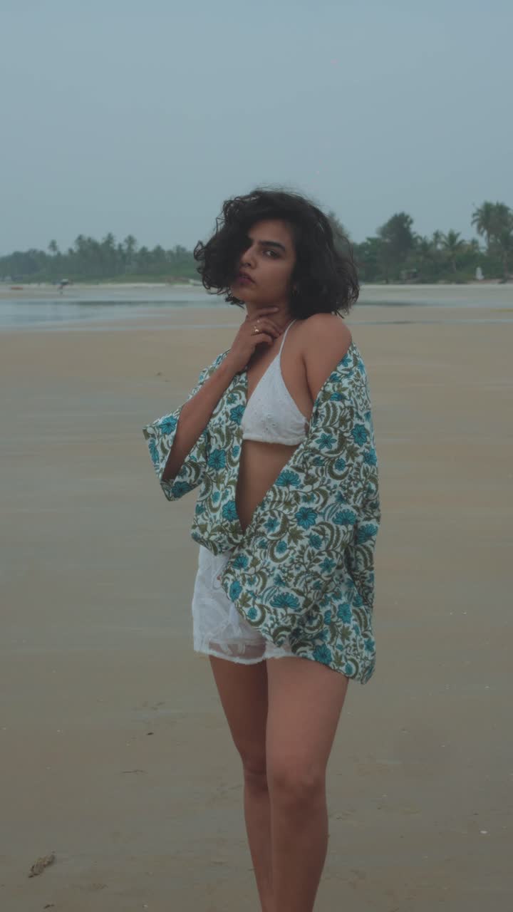 Young woman on a tropical beach adjusting her curly hair, creating a natural and confident pose, radiating summer spirit and beach vacation leisure