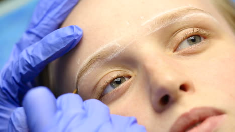 beautician doing eyebrow tattooing for female face
