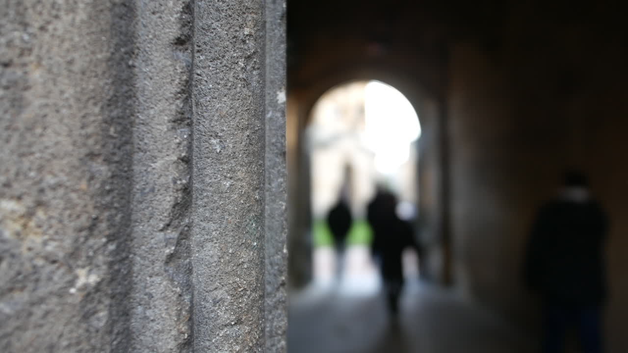 A shallow depth of field shot captures blurred pedestrians walking through an ancient stone archway ideal for evoking historical ambiance in travel architecture or urban exploration projects