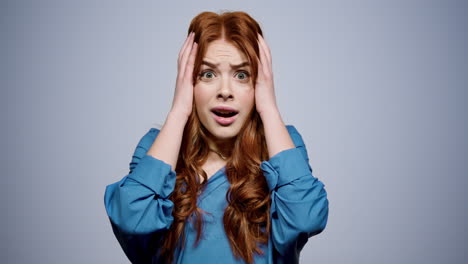 shocked girl holding head with hands in studio. frustrated woman posing on gray