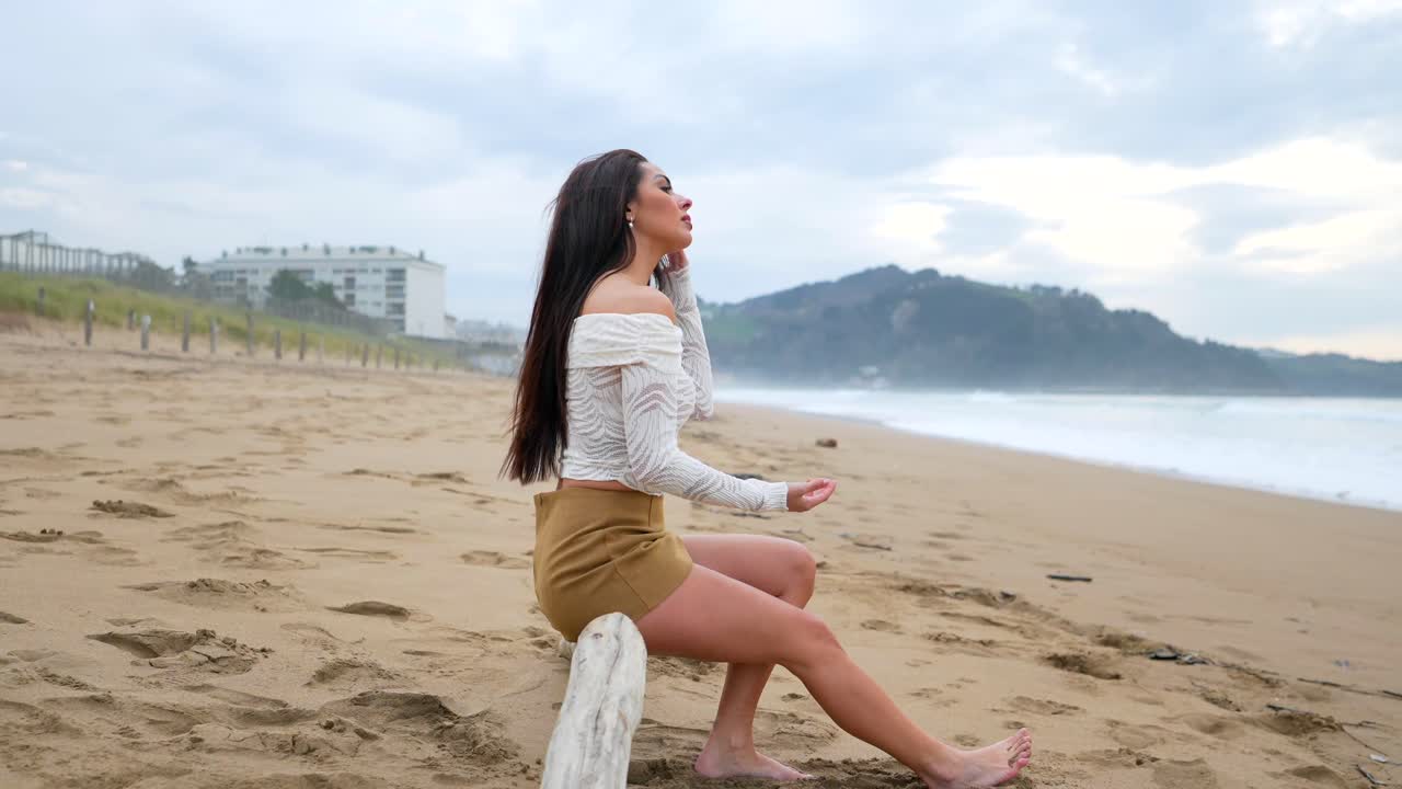 Woman sitting on driftwood at the beach