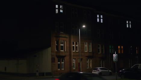 Street-light-flashes-above-speed-limit-sign-as-tall-lamp-illuminates-road-below-apartment-buildings-at-night