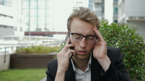 hombre serio hablando por teléfono afuera, mirando decepcionado