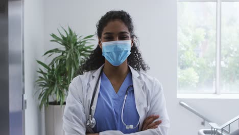 Portrait-of-asian-female-doctor-wearing-face-mask-standing-with-arms-crossed-in-hospital