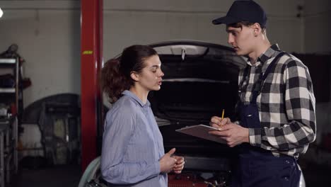 joven atractiva propietaria de un coche explica al técnico de automóviles todas sus quejas sobre su vehículo y firma algo en