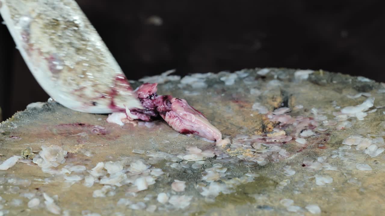 Mani che squamano abilmente pesce fresco con un coltello su un tagliere rustico, mercato filippino.