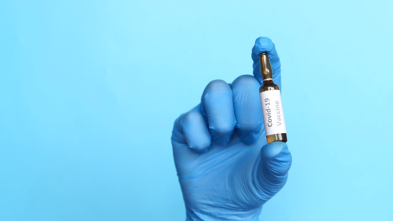 mano con guante azul sosteniendo el vial de la vacuna covid-19