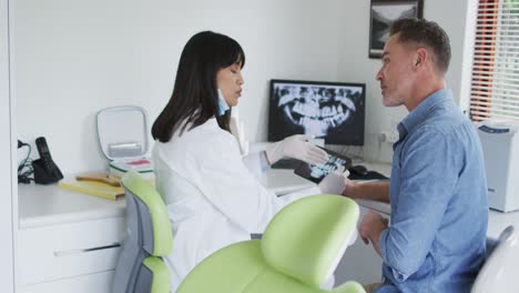 biracial female dentist with face mask examining teeth of male patient at modern dental clinic