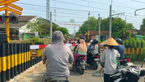 People with their vehicles are stopped in front of the railway crossing. Waiting for the train to pass. Indonesia.