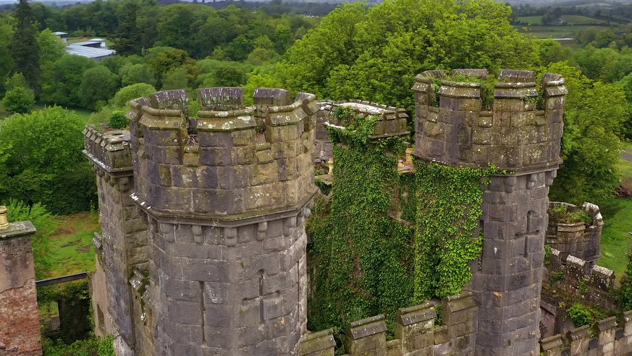 Vista aerea al rallentatore che orbita intorno alle torri gemelle del Castello Saunderson con un paesaggio verde lussureggiante e dettagli di fortificazione