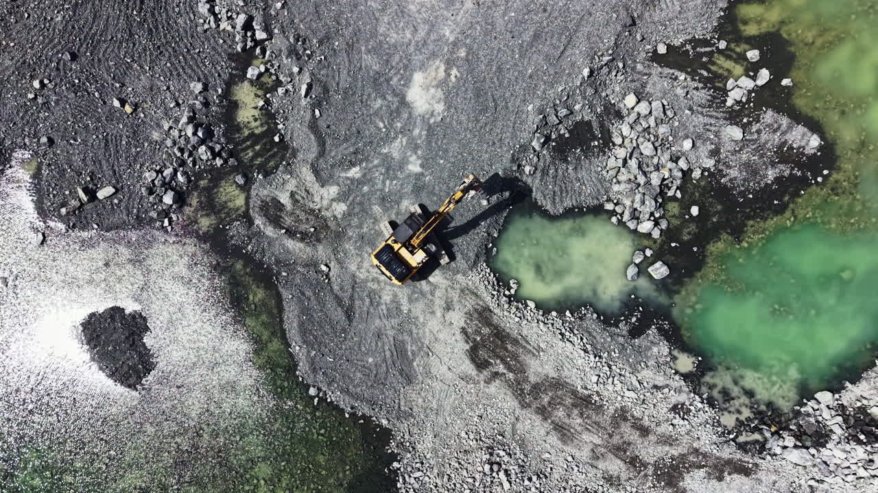 Granite quarry operation with large machinery near water in a rugged landscape during daylight hours