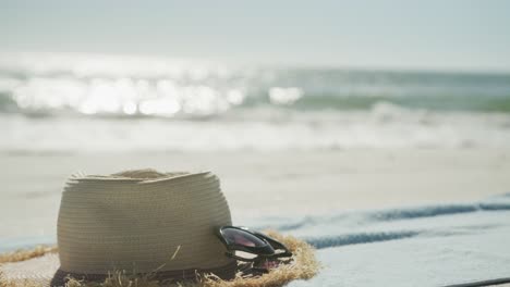 close up of straw hat, sunglasses and towel on beach, in slow motion, with copy space