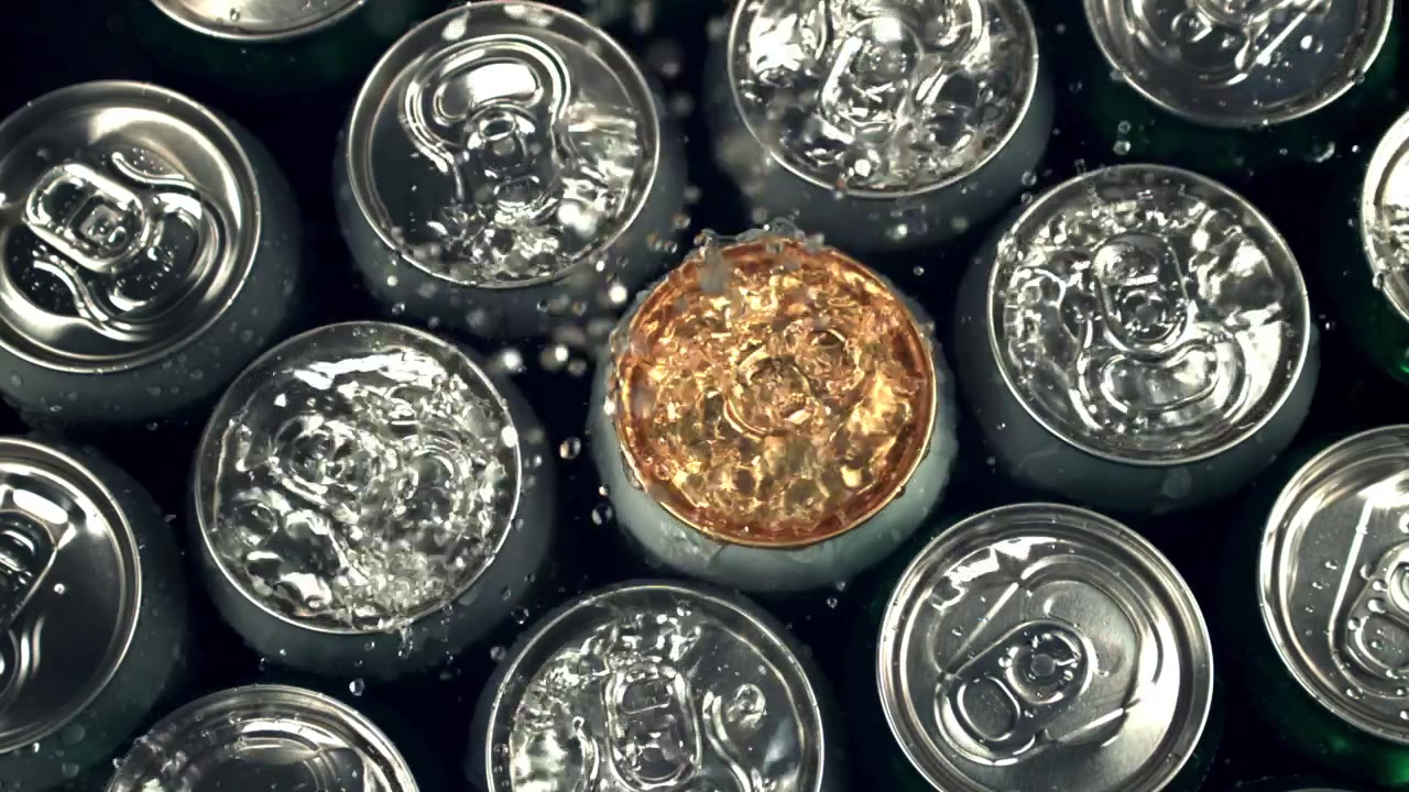 Agua salpicando latas de bebidas frías con líquido dorado
