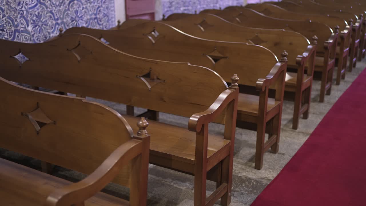 Wooden church pews with decorative carvings, aligned beside a red carpet aisle, emphasizing the serene atmosphere