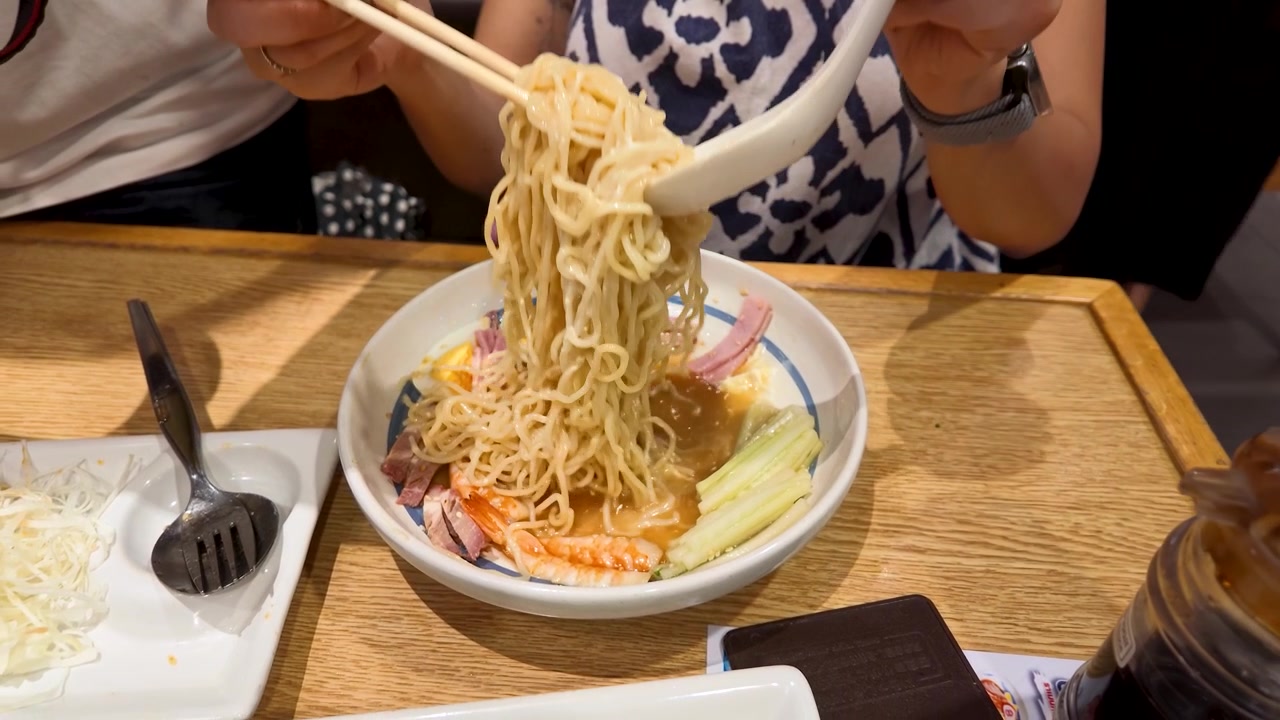 Primo piano di una donna che usa bacchette e cucchiaio per mangiare ramen in un ristorante luminoso