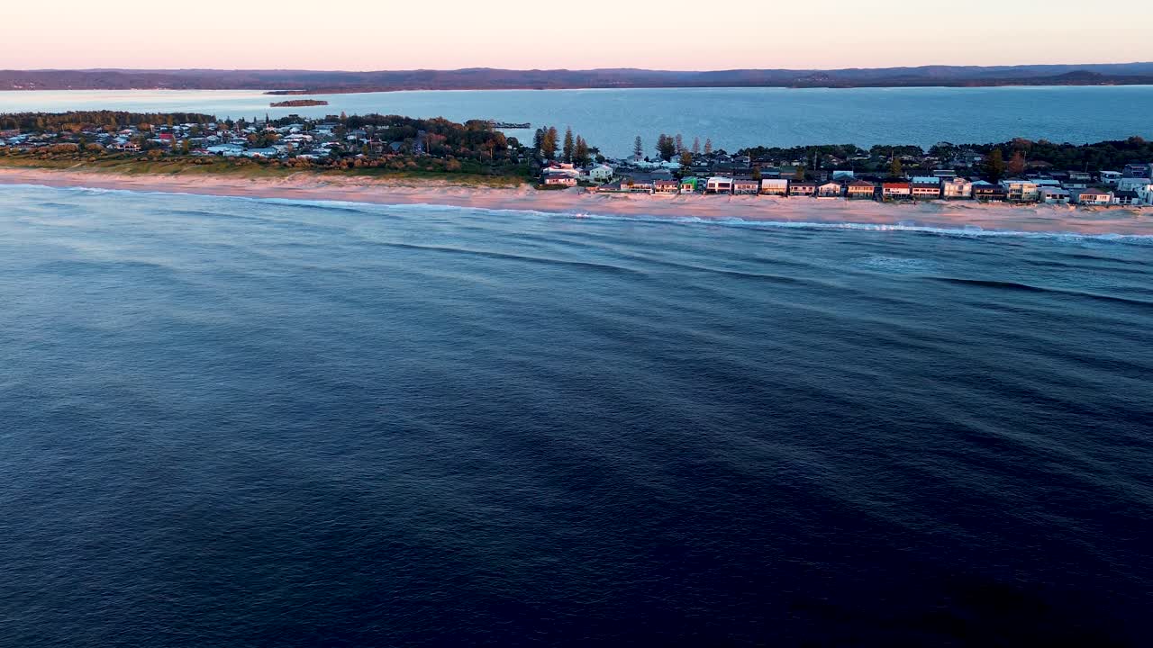 Drone aerial landscape of waves breaking on ocean coastline sandbar beach with street and residential housing town suburbs of North Entrance and Tuggerah Lakes on Central Coast Australia travel bay