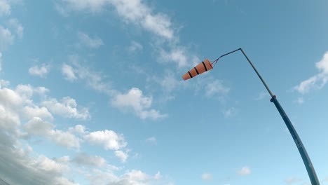 looking up at slow motion striped airport windsock blowing against blue cloudy sky