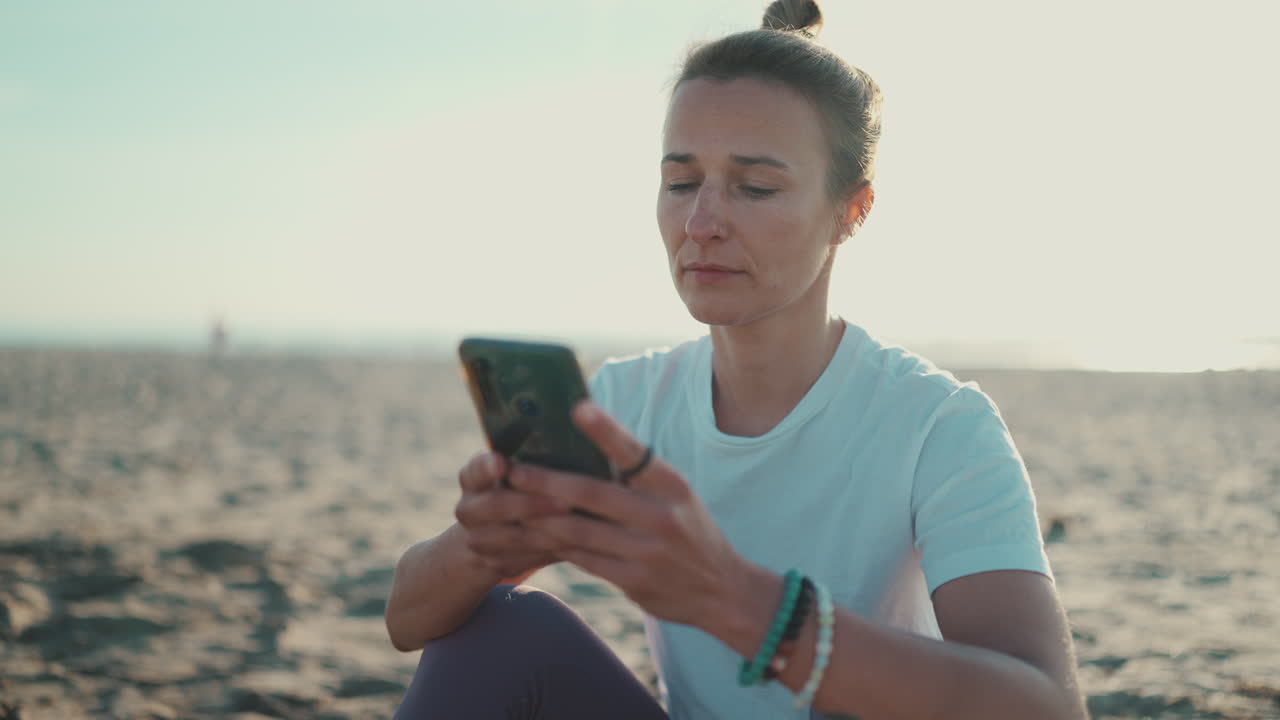 una deportista sentada usando su teléfono inteligente en la playa.
