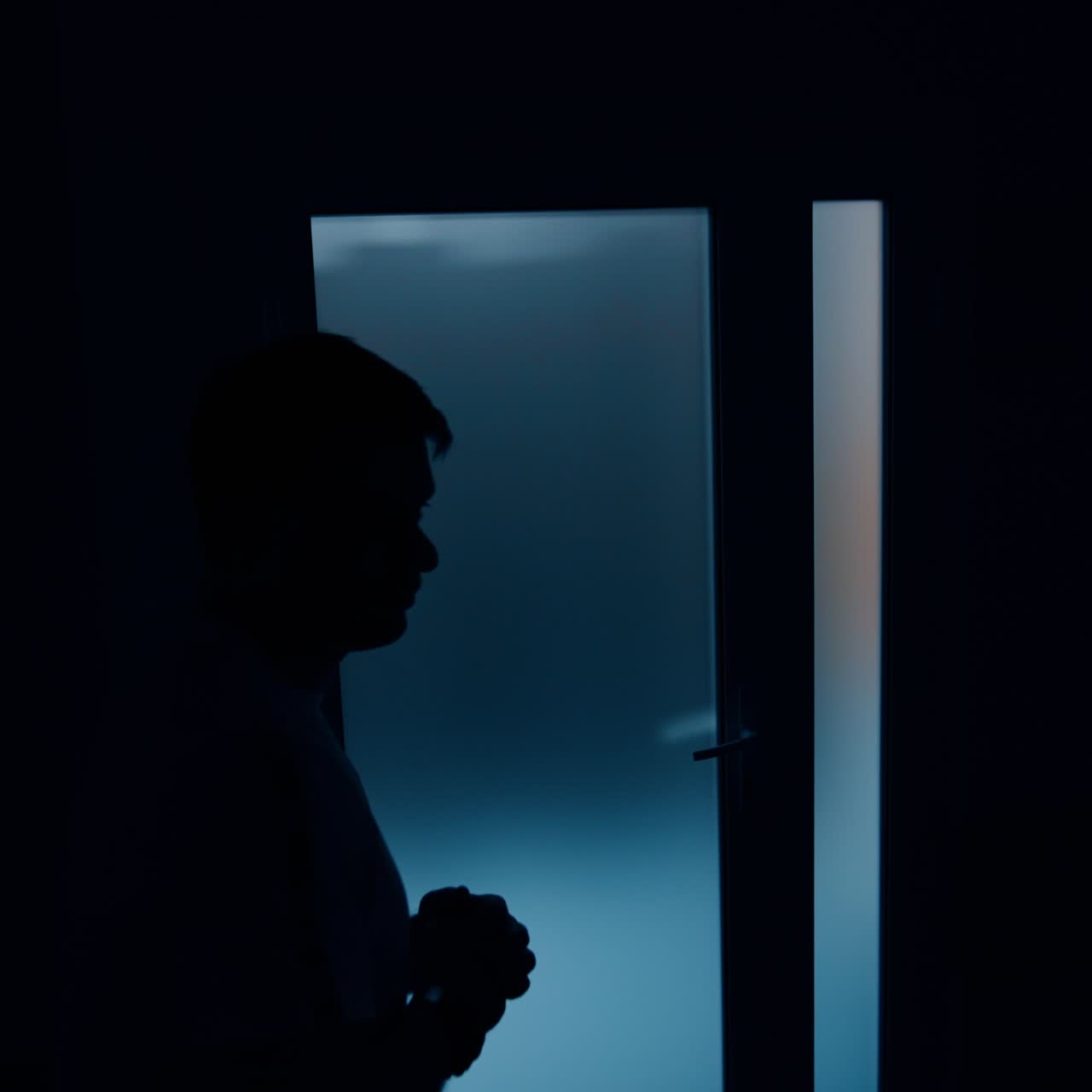Male silhouette moving in the dark room in front of light door. Man worries while his wife is delivering a baby. Top view