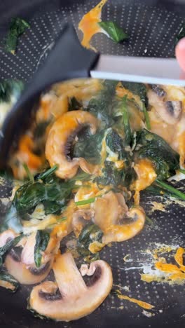 cooking scrambled eggs with spinach and mushrooms in a frying pan
