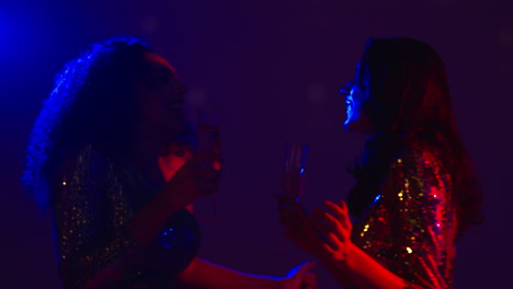 close up of two women in nightclub or bar celebrating doing cheers and drinking alcohol 1