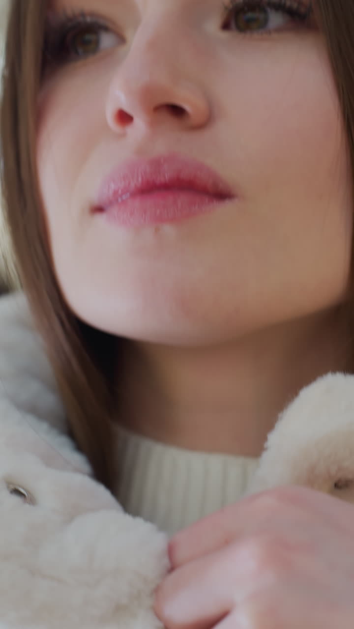 Close-up of woman hands zipping up a soft, fluffy winter jacket with a blurred background featuring warm bokeh lights, cozy outerwear fashion for cold weather in a stylish seasonal setting
