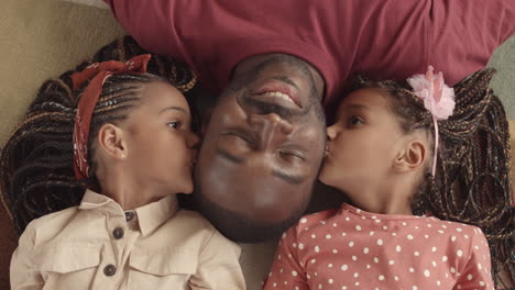 sisters kissing dad lying on floor