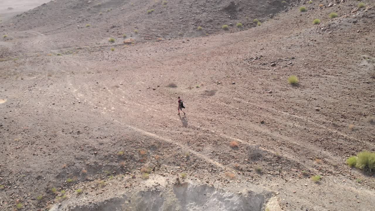 Ripresa aerea in tracking da drone di un giovane uomo che cammina in valli desertiche rocciose a Hatta, Emirati Arabi Uniti