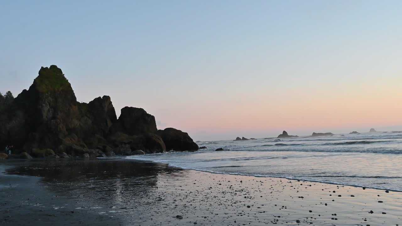 Aerial drone view of rugged sea stacks reflecting on a wet beach at sunset