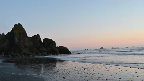 aerial drone view of rugged sea stacks reflecting on a wet beach at sunset