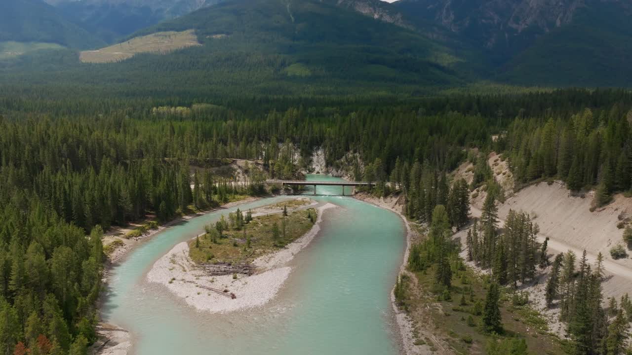 tomada de un avión no tripulado del río kootenay con una carretera de tala al lado y un puente que lo cruza con montañas en el fondo en un día soleado en columbia británica, canadá