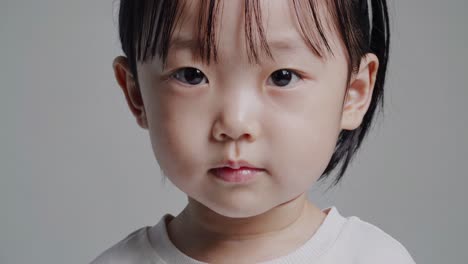 retrato en primer plano de un adorable niño joven de asia oriental con cabello oscuro y ojos mirando directamente a la cámara contra un fondo gris neutro, transmitiendo una sensación de inocencia y curiosidad