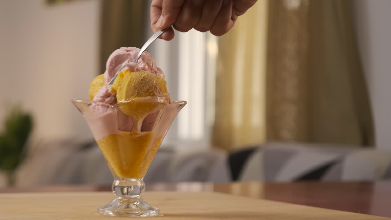 A man hand holding a spoon while eating delicious and tasty ice cream from a glass cup. Summer and sugar concept.