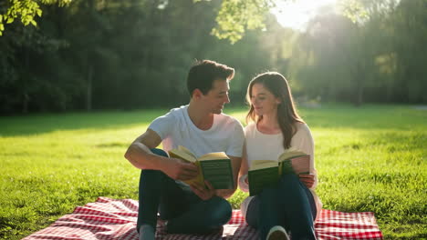 young couple reading books together on a picnic blanket in a sunny park