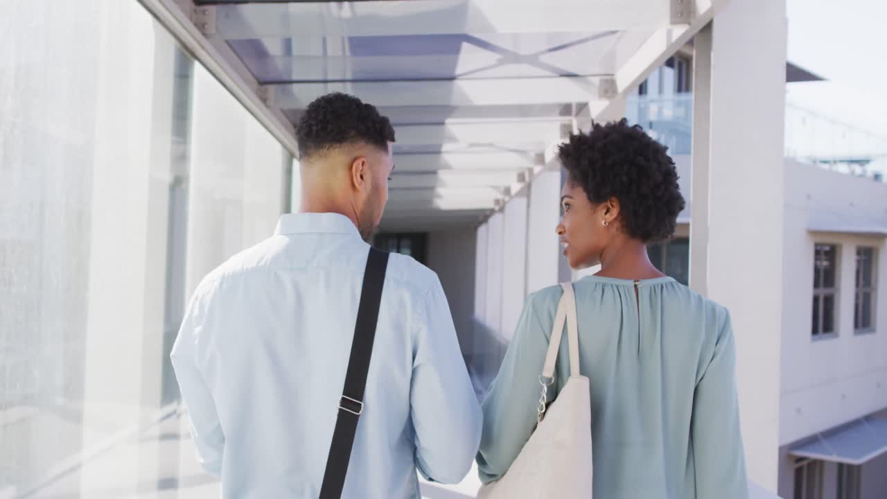 Video of back view of diverse businessman and businesswoman walking and talking