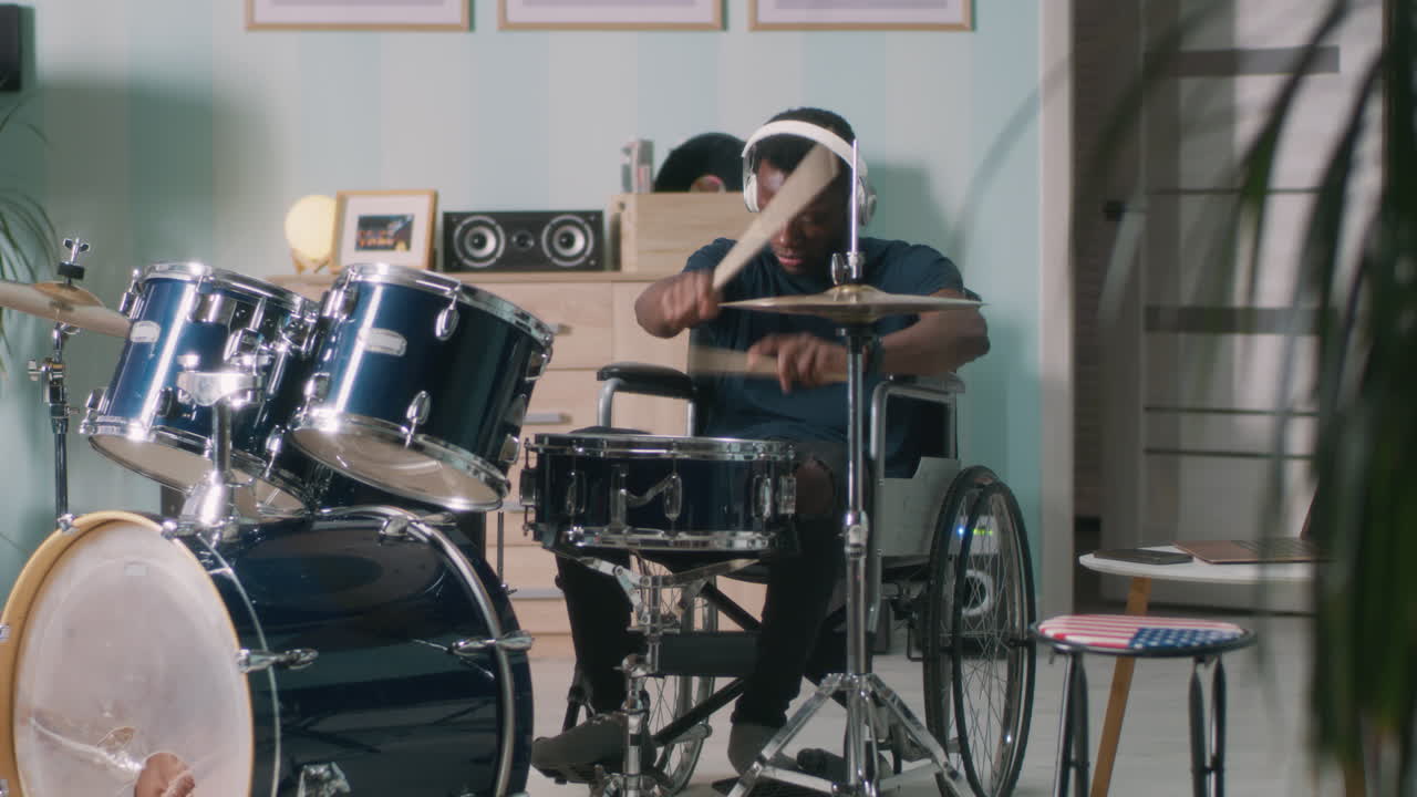 Black Man in Wheelchair Playing Guitar and Singing in Mic at Home Shot of African American Man in Headphones Sitting in Wheelchair at Home Playing Guitar and Singing in Microphone