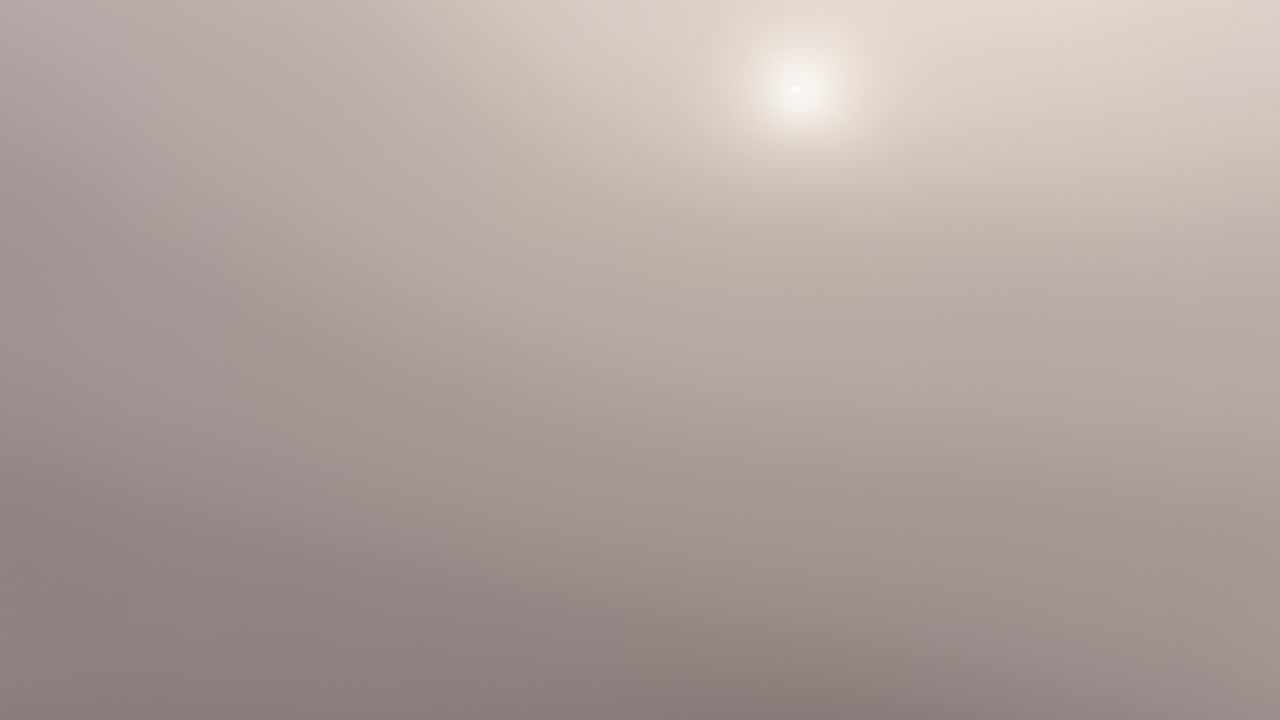 An aerial view reveals a residential area in Weesen and the serene Walensee Lake as a drone passes through a foggy and misty layer. The tranquil lake and peaceful village emerge from the mist.