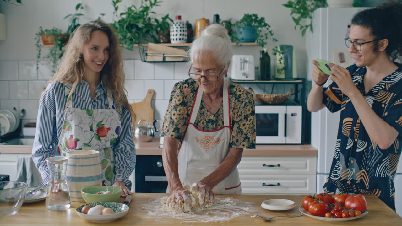 Ragazzo che filma la nonna mentre impasta durante il tempo di cucina in famiglia