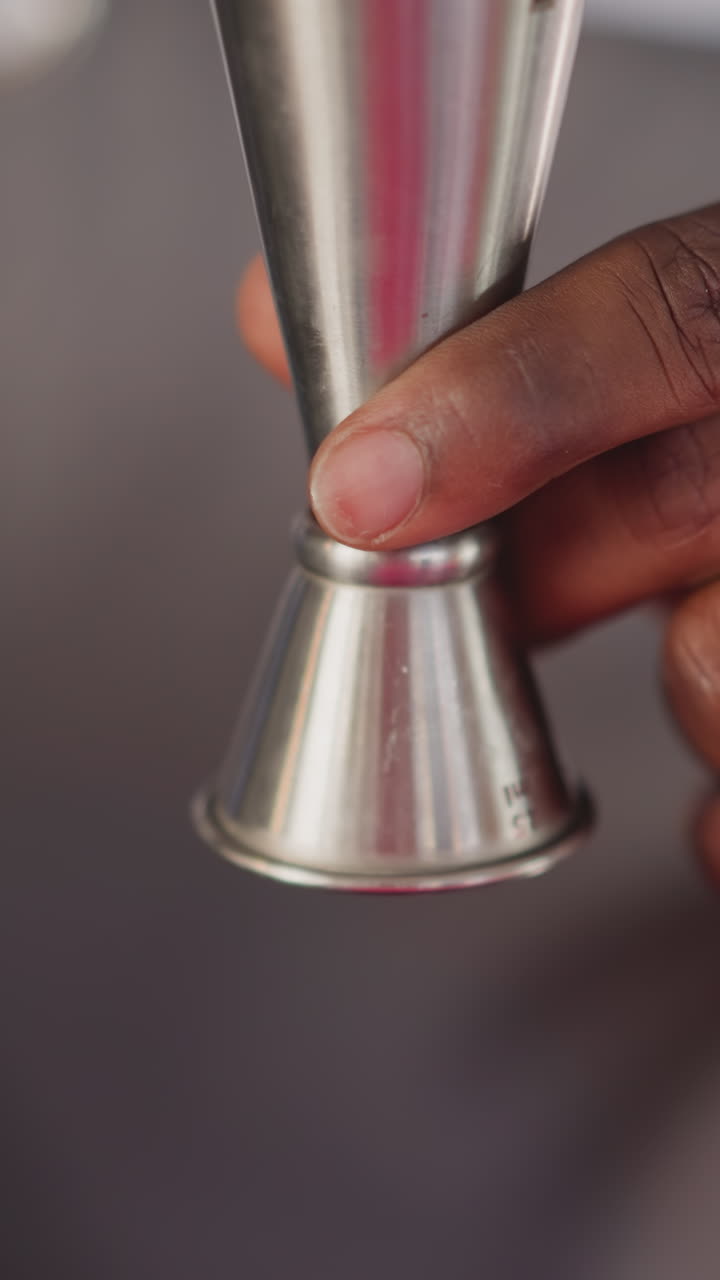 Barman pours juice into jigger in bar closeup. Black bartender measures ingredient for refreshing cocktail in club. Barkeeper makes exotic drink
