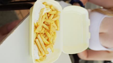 woman opens a plastic takeaway container with french fries, vertical