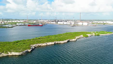 Drone-push-in-over-white-tropical-rocks-with-green-grass-to-establish-oil-refinery-in-background